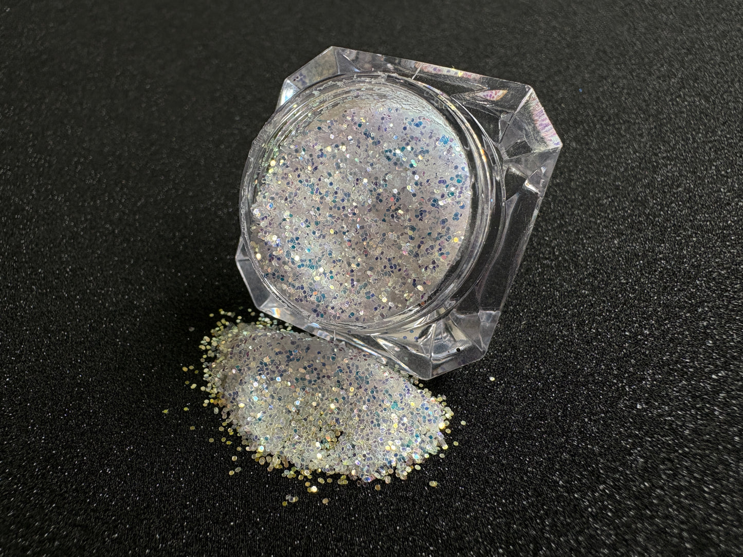 Blue-purple and gold glitter mix spilled from a clear jar onto a black textured background.