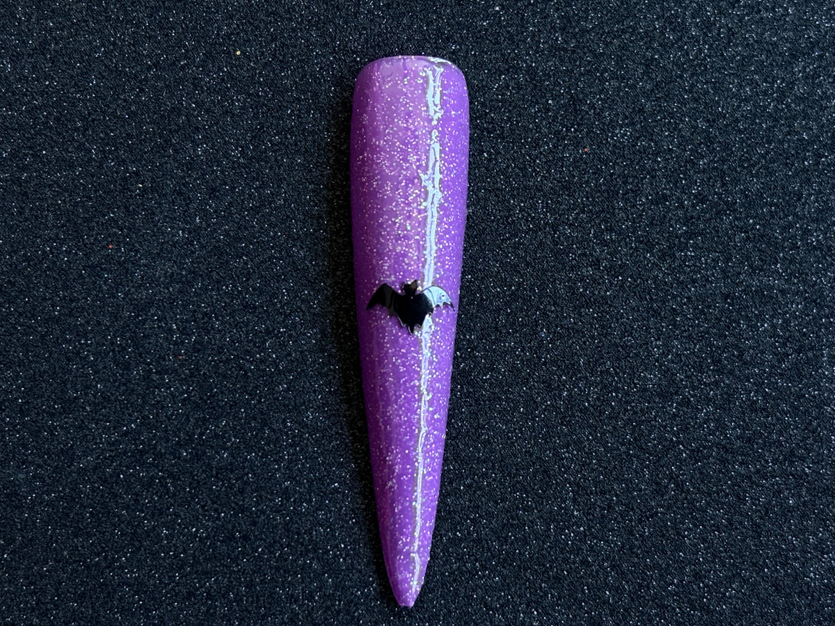 Black bat Halloween nail sticker applied on a sparkly purple stiletto nail tip against a black textured background.