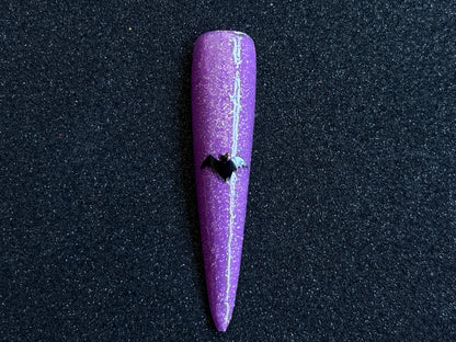 Black bat Halloween nail sticker applied on a sparkly purple stiletto nail tip against a black textured background.