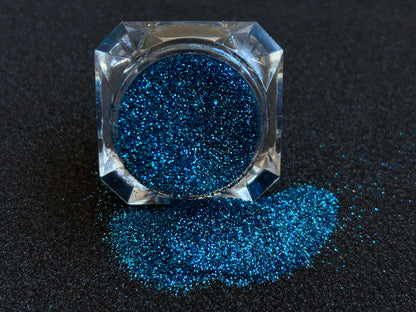 Blue and teal glitter mix spilled from a clear jar onto a black textured background.