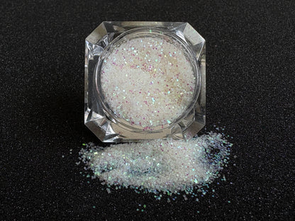 Iridescent white glitter spilled from a clear jar onto a black textured background.