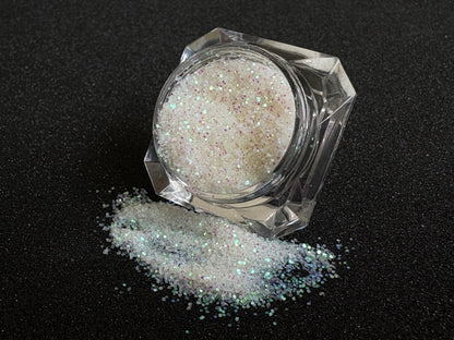 Iridescent white glitter spilled from a clear jar onto a black textured background.