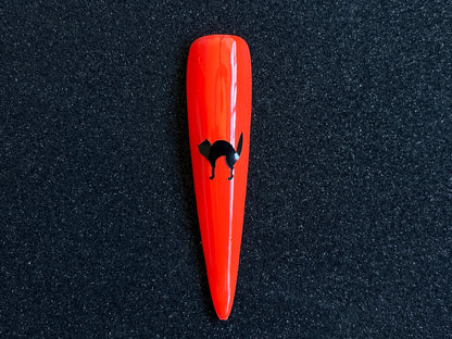 Black cat Halloween nail sticker applied on a bright orange stiletto nail tip against a black textured background.