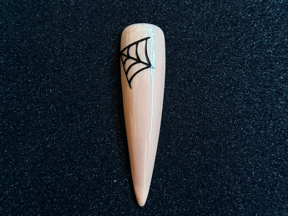 Black cobweb Halloween nail sticker applied on a glossy nude stiletto nail tip against a black textured background.