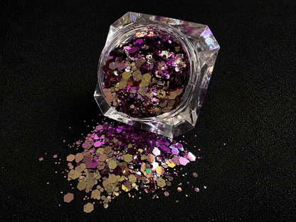 Purple super chunky glitter mix with pale gold colour-shifting sparkle spilled from a clear jar onto a black textured background.
