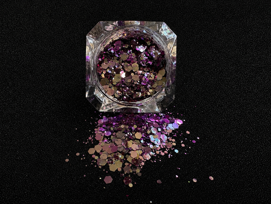 Purple super chunky glitter mix with pale gold colour-shifting sparkle spilled from a clear jar onto a black textured background.
