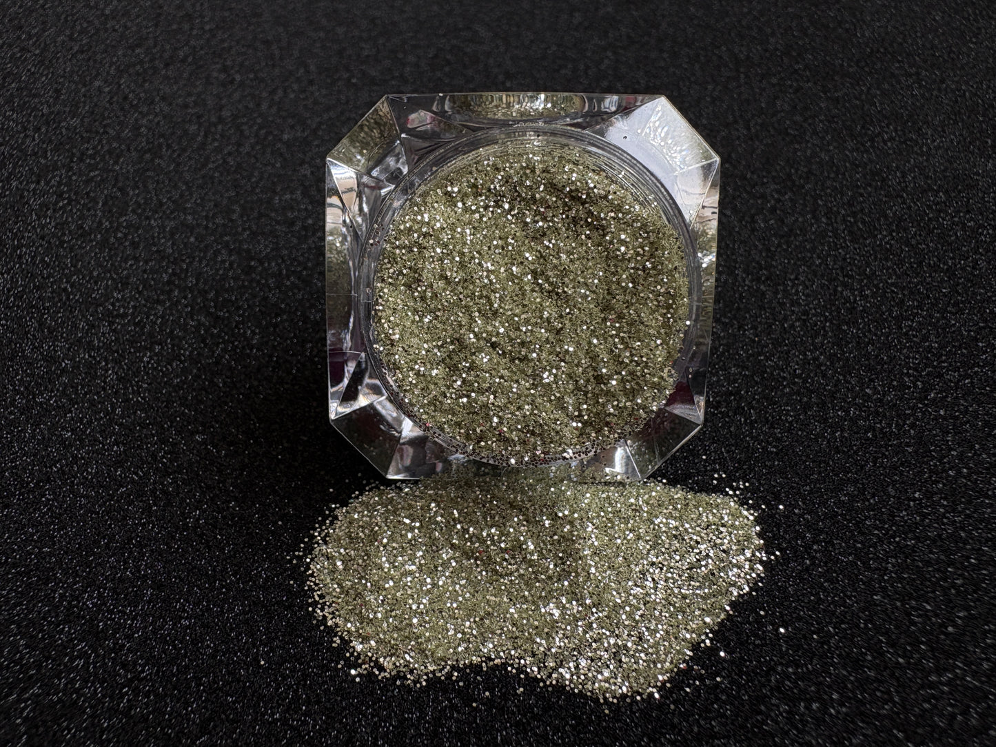 Champagne gold and silver glitter mix spilled from a clear jar onto a black textured background.