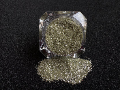 Champagne gold and silver glitter mix spilled from a clear jar onto a black textured background.