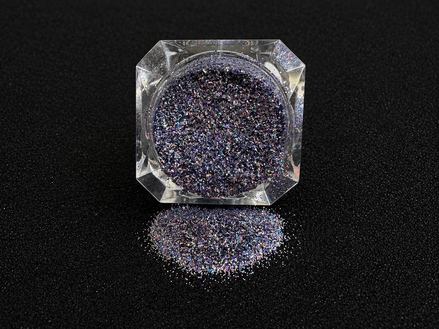 Holographic silver blue glitter in a clear jar, tilted back and forth to show sparkle against a black background.