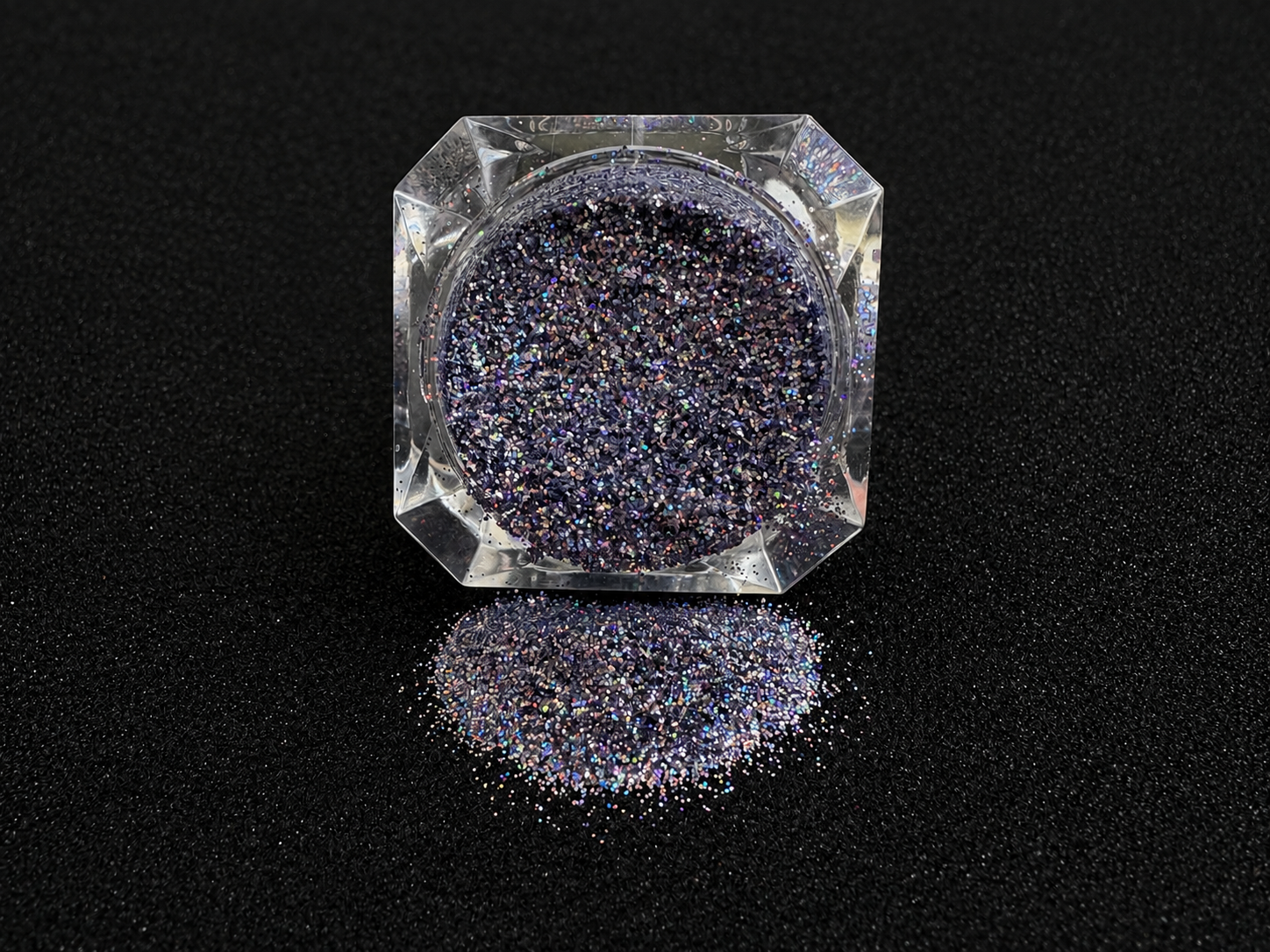 Holographic silver blue glitter in a clear jar, tilted back and forth to show sparkle against a black background.