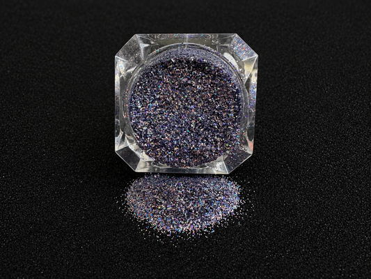 Holographic silver blue glitter in a clear jar, tilted back and forth to show sparkle against a black background.
