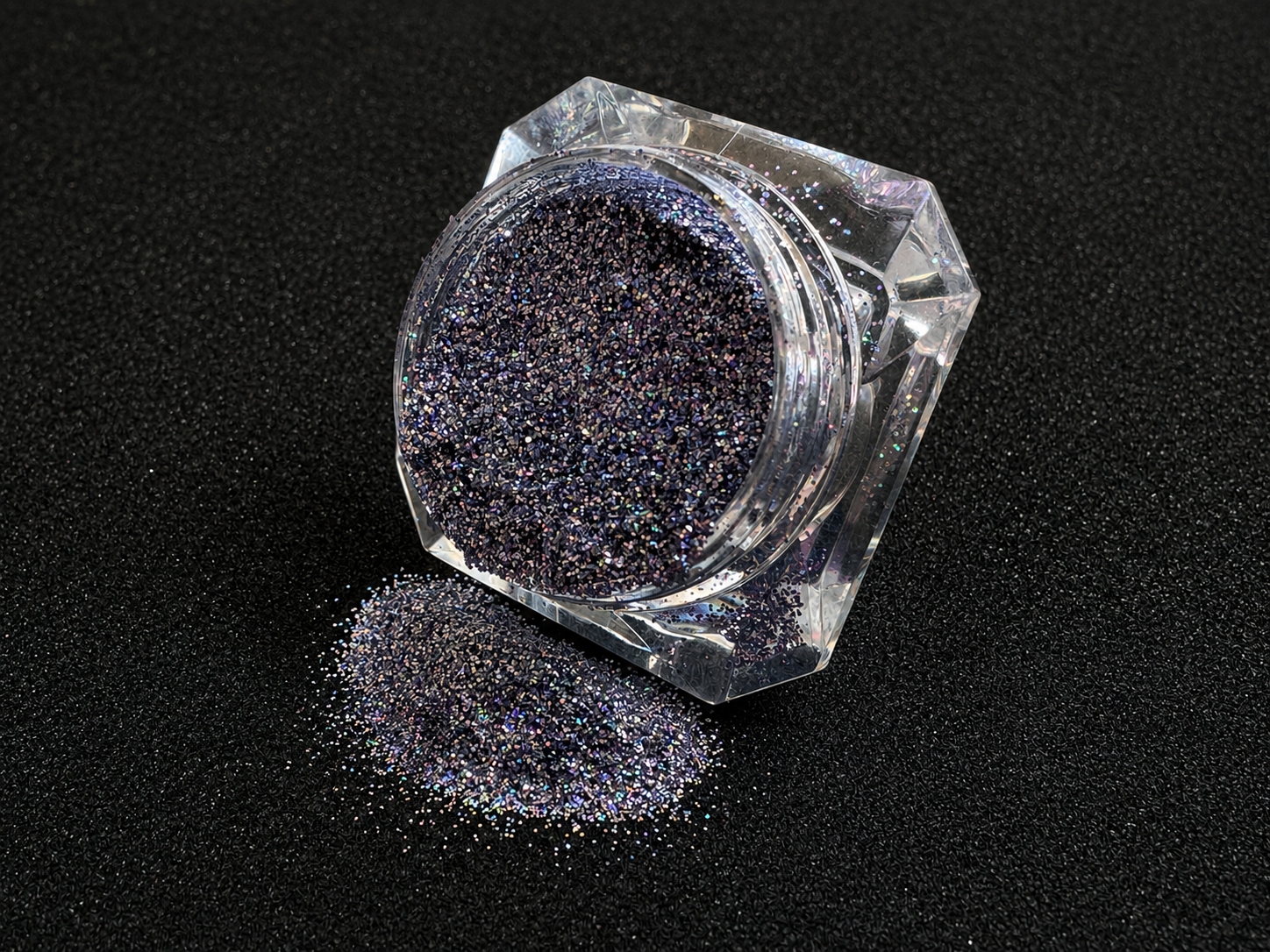 Holographic silver blue glitter in a clear jar, tilted back and forth to show sparkle against a black background.