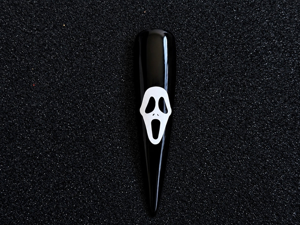 White Ghostface Halloween nail sticker applied on a glossy black stiletto nail tip against a black textured background.