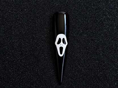 White Ghostface Halloween nail sticker applied on a glossy black stiletto nail tip against a black textured background.