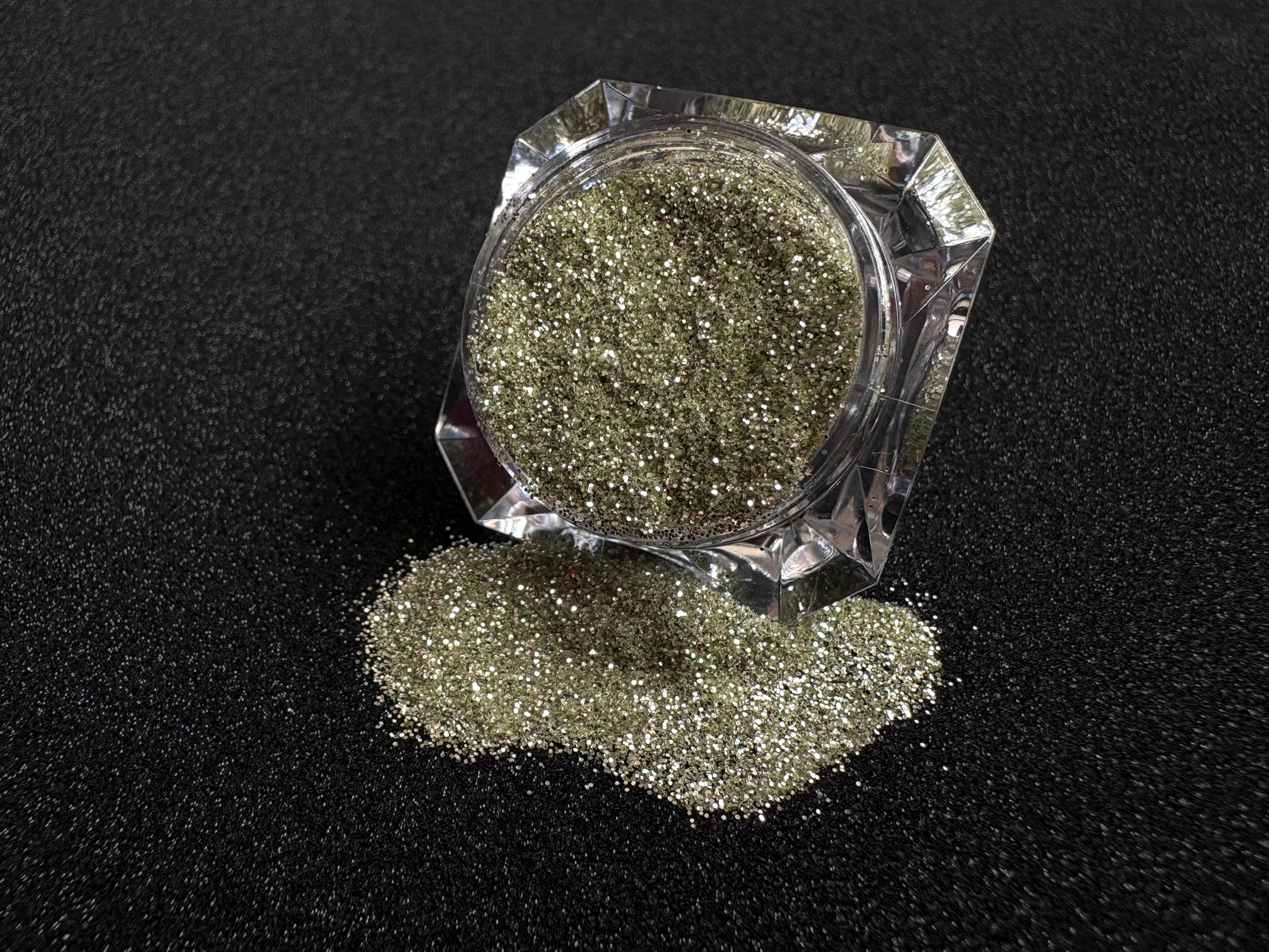 Champagne gold and silver glitter mix spilled from a clear jar onto a black textured background.