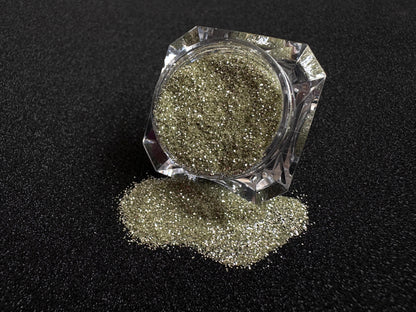 Champagne gold and silver glitter mix spilled from a clear jar onto a black textured background.