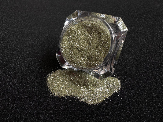 Champagne gold and silver glitter mix spilled from a clear jar onto a black textured background.
