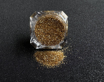 Gold metallic glitter spilled from a clear jar onto a black textured background.