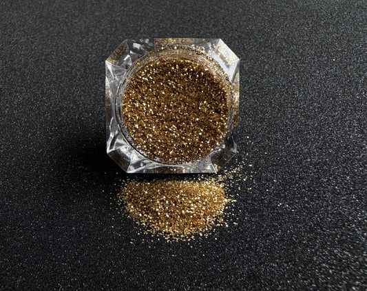 Gold metallic glitter spilled from a clear jar onto a black textured background.