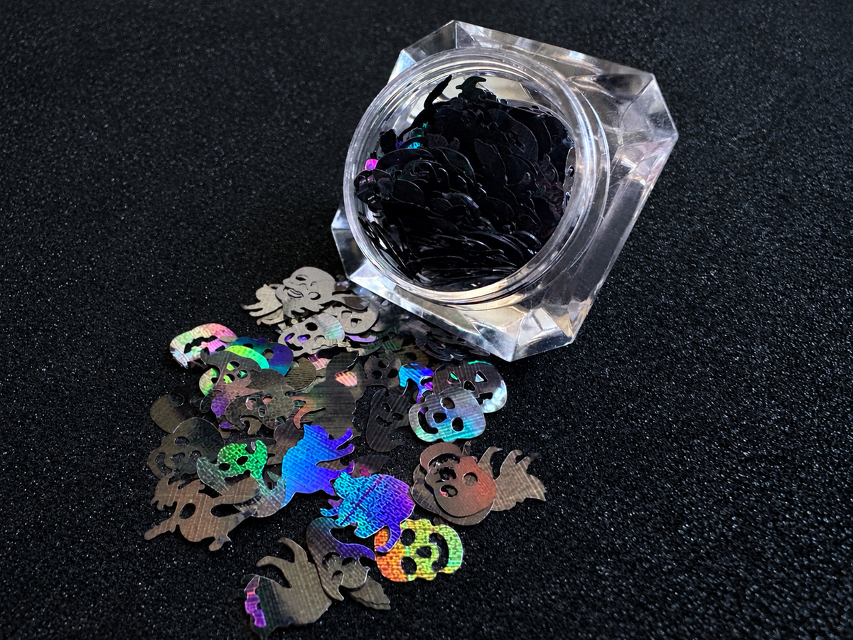 Holographic black Halloween glitter shapes featuring pumpkins, skulls, ghosts, cats, bats, and witches spilled from a clear jar onto a black textured background.