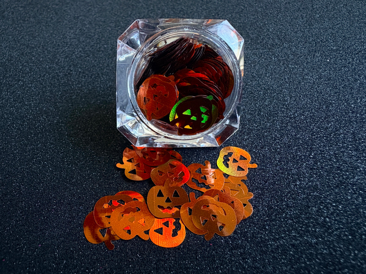 10mm holographic brown pumpkin glitter shapes spilled from a clear jar onto a black textured background.