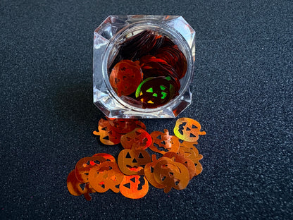 10mm holographic brown pumpkin glitter shapes spilled from a clear jar onto a black textured background.