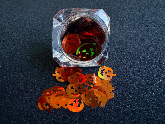 10mm holographic brown pumpkin glitter shapes spilled from a clear jar onto a black textured background.