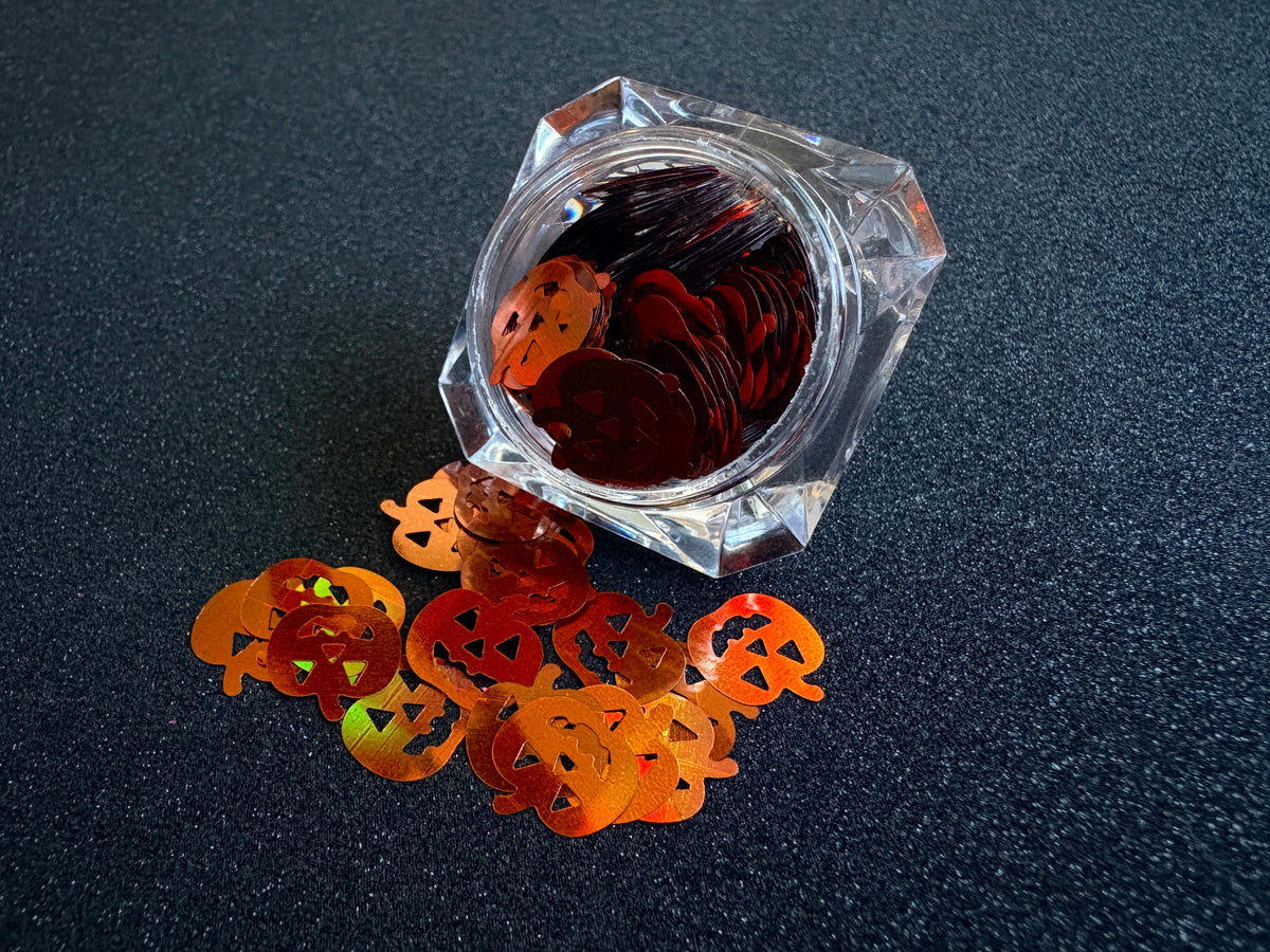 10mm holographic brown pumpkin glitter shapes spilled from a clear jar onto a black textured background.