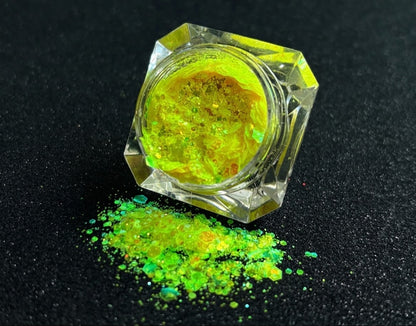 Fluorescent iridescent green super chunky glitter mix with yellow shift spilled from a clear jar onto a black textured background.
