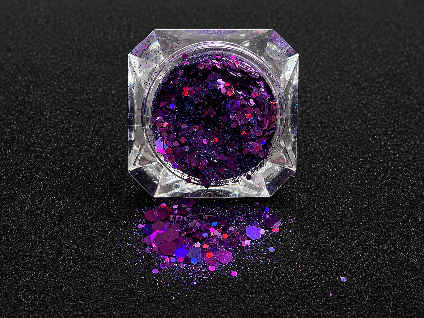 Deep purple and violet super chunky glitter mix with holographic sparkle spilled from a clear jar onto a black textured background.