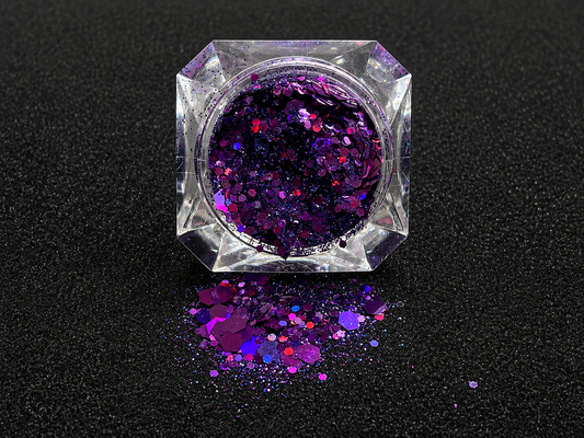 Deep purple and violet super chunky glitter mix with holographic sparkle spilled from a clear jar onto a black textured background.