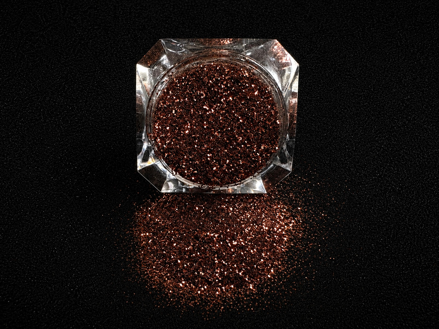 Chocolate brown metallic glitter spilled from a clear jar onto a black textured background.