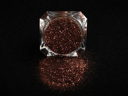Chocolate brown metallic glitter spilled from a clear jar onto a black textured background.