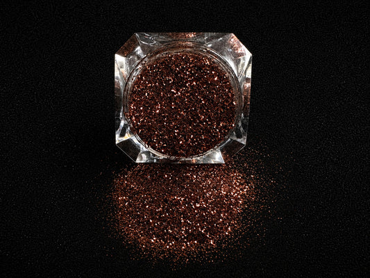 Chocolate brown metallic glitter spilled from a clear jar onto a black textured background.