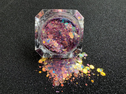 Top-down view of super chunky pastel purple glitter mix with rose gold iridescent colour shift, spilled from a clear jar onto a black textured background.
