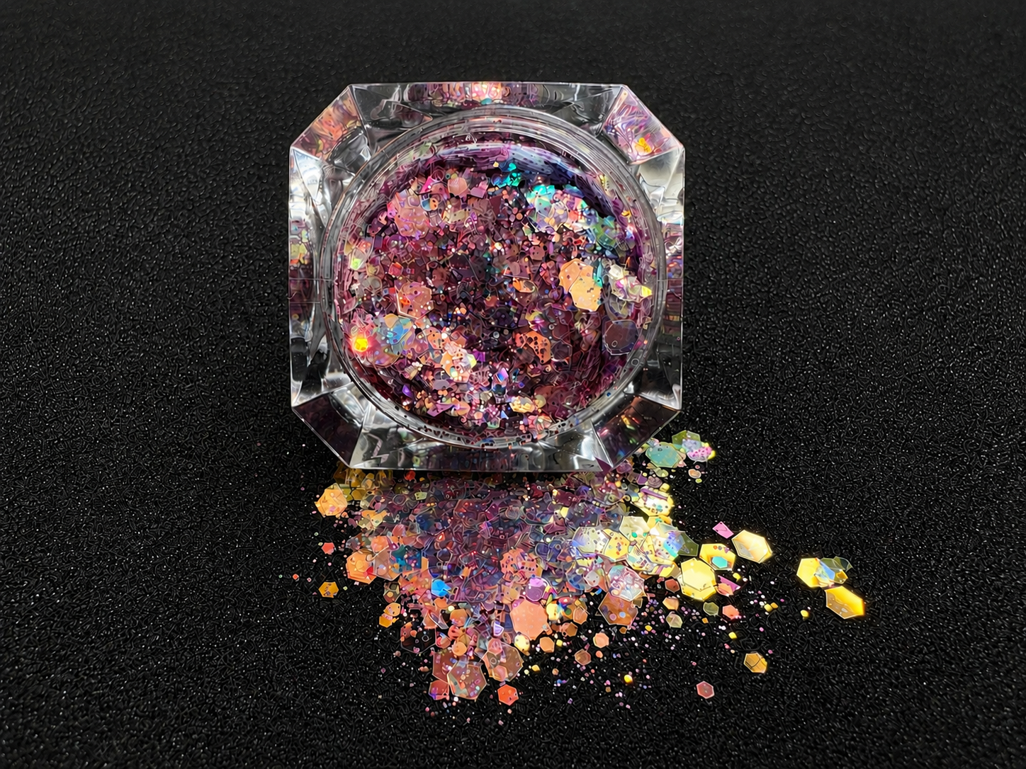 Top-down view of super chunky pastel purple glitter mix with rose gold iridescent colour shift, spilled from a clear jar onto a black textured background.