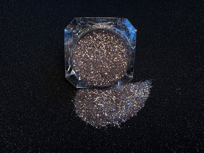 Champagne pink glitter spilled from a clear jar onto a black textured background.