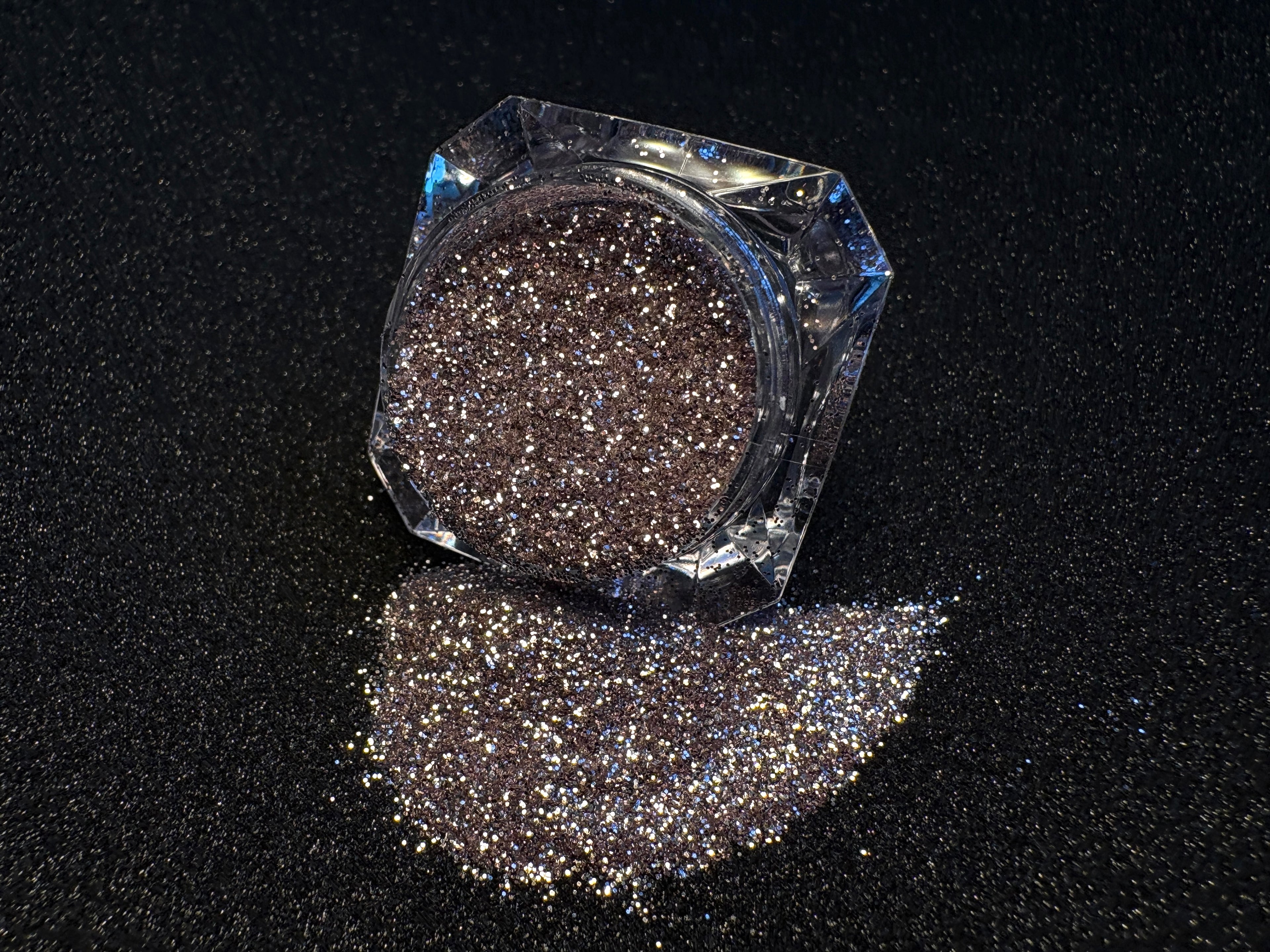 Champagne pink glitter spilled from a clear jar onto a black textured background.