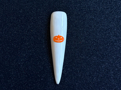 Orange pumpkin Halloween nail sticker applied on a glossy white stiletto nail tip against a black textured background.