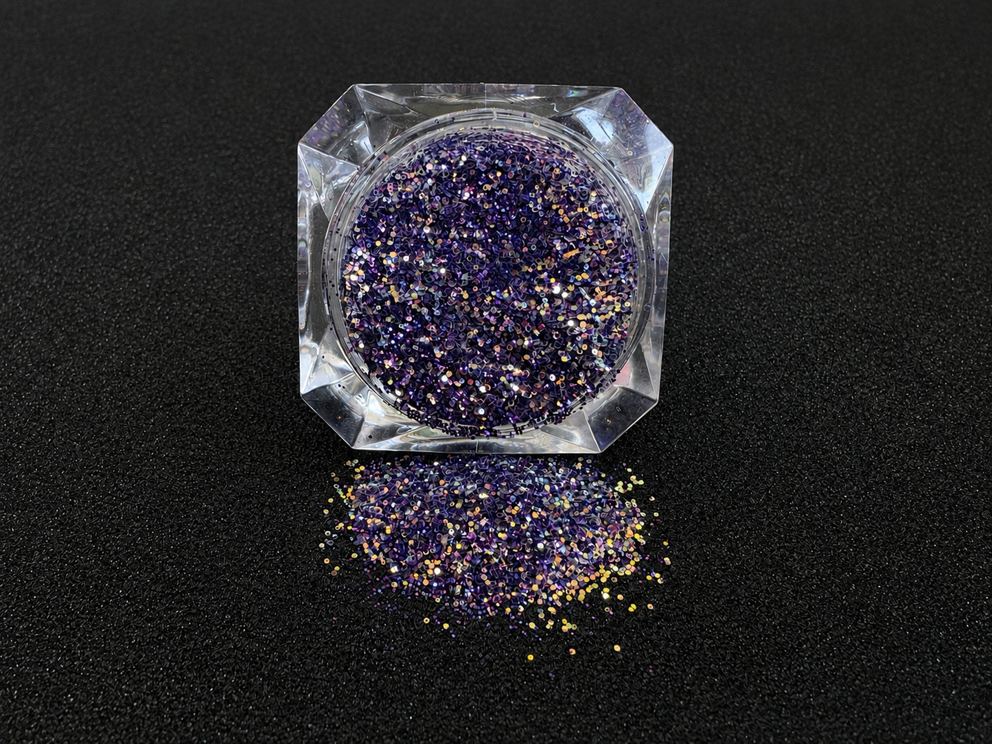 Purple and gold glitter mix spilled from a clear jar onto a black textured background.