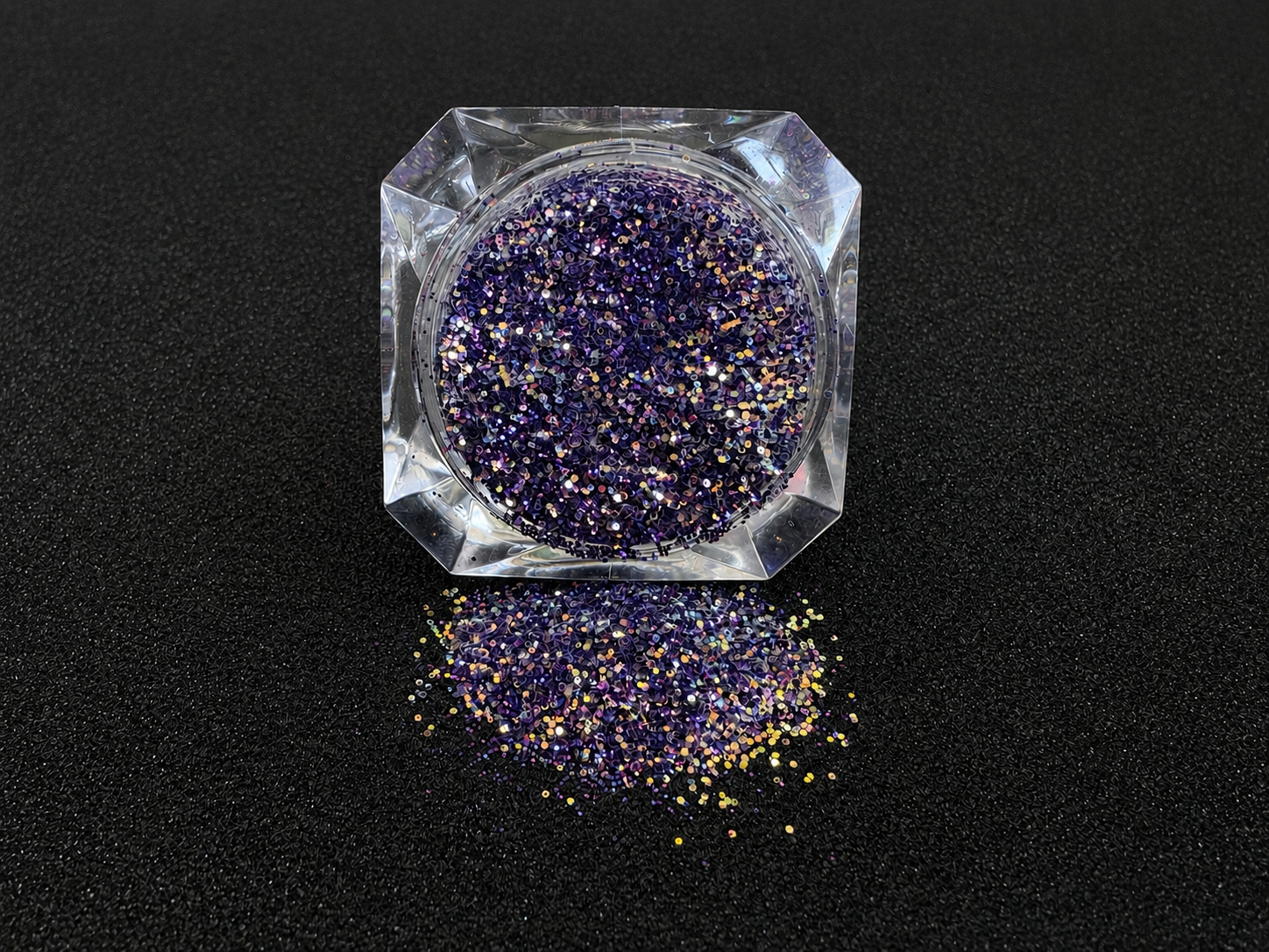 Purple and gold glitter mix spilled from a clear jar onto a black textured background.