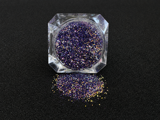 Purple and gold glitter mix spilled from a clear jar onto a black textured background.