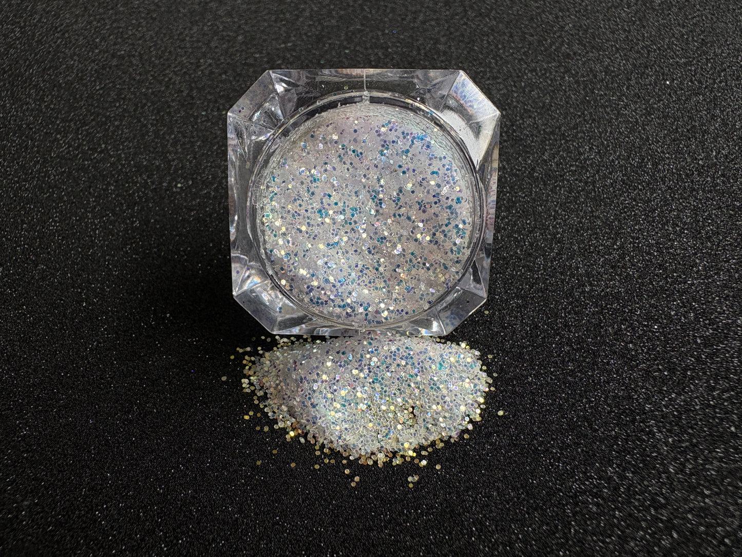 Blue-purple and gold glitter mix spilled from a clear jar onto a black textured background.