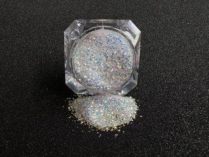 Blue-purple and gold glitter mix spilled from a clear jar onto a black textured background.