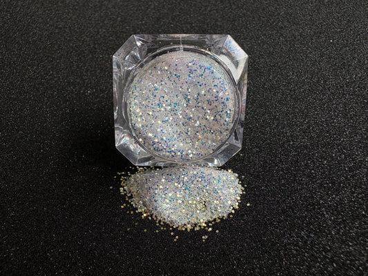 Blue-purple and gold glitter mix spilled from a clear jar onto a black textured background.