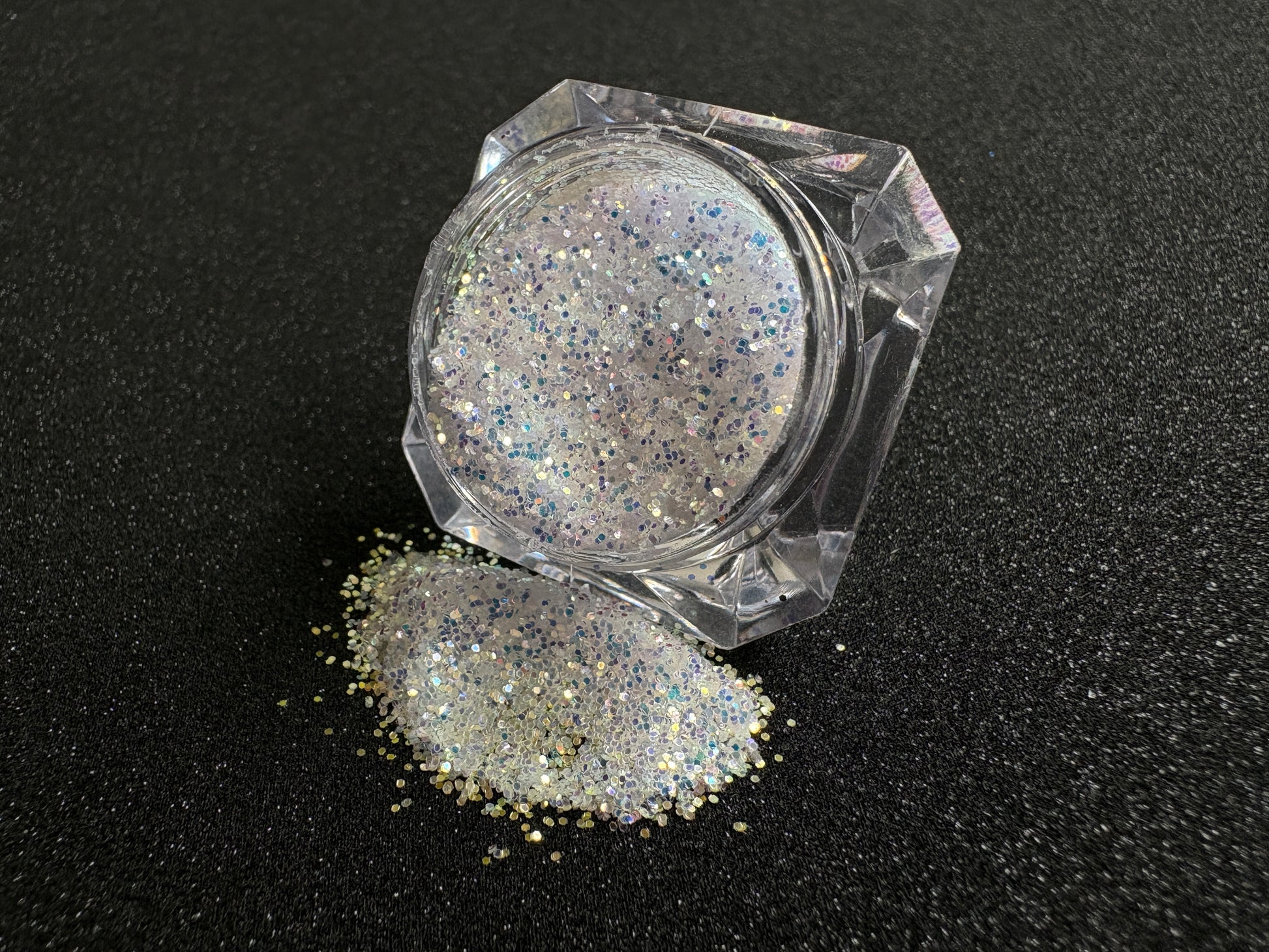 Blue-purple and gold glitter mix spilled from a clear jar onto a black textured background.