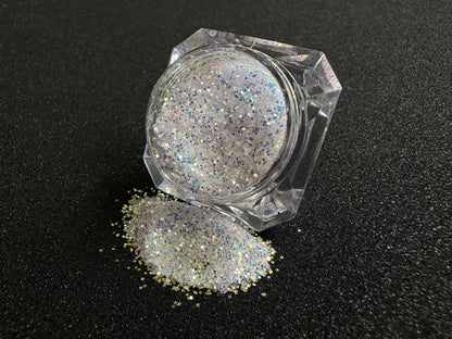 Blue-purple and gold glitter mix spilled from a clear jar onto a black textured background.