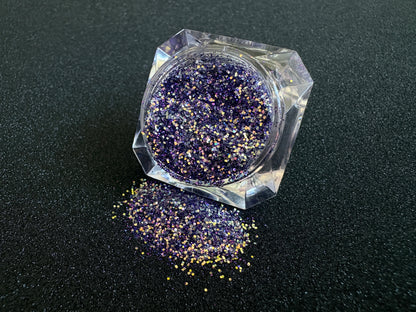 Purple and gold glitter mix spilled from a clear jar onto a black textured background.