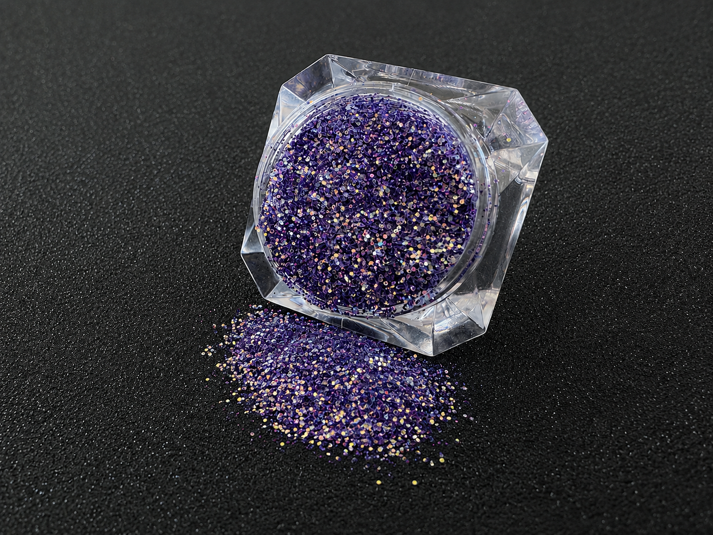 Purple and gold glitter mix spilled from a clear jar onto a black textured background.