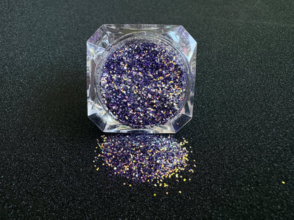 Purple and gold glitter mix spilled from a clear jar onto a black textured background.